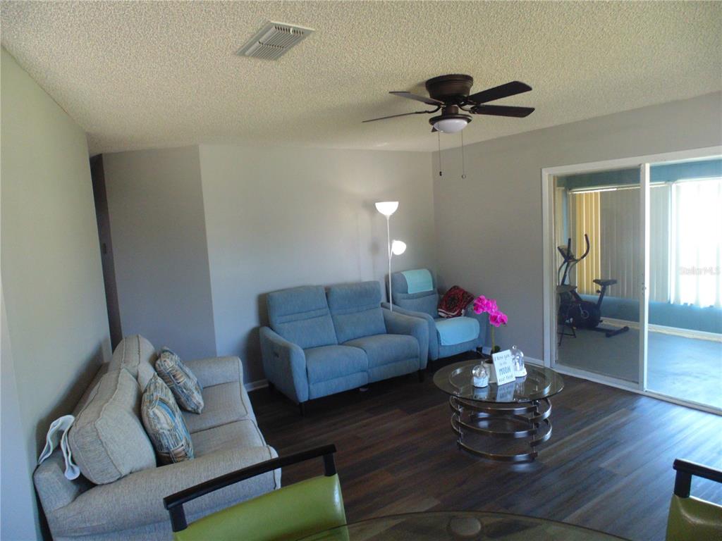 A living room features a beige sofa, blue loveseat, glass coffee table, and dark flooring — 10210 SW 93RD AVENUE, OCALA, FL