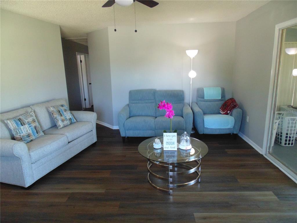 A living room features light gray walls, dark wood-look flooring, and blue upholstered seating — 10210 SW 93RD AVENUE, OCALA, FL