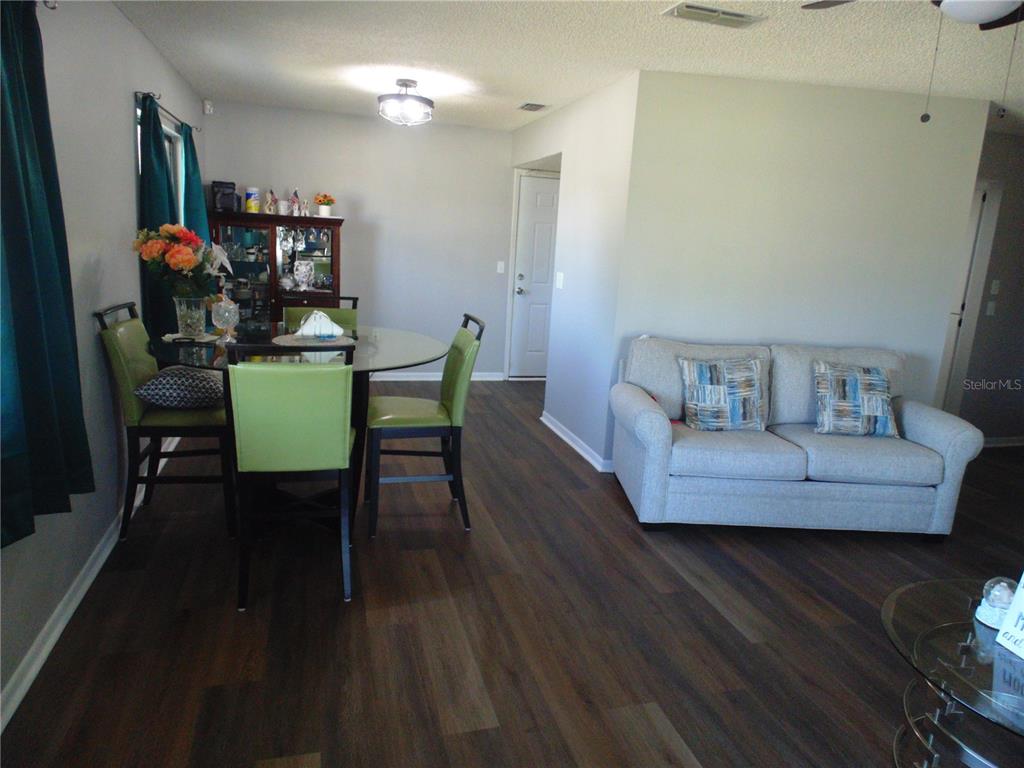 A dining area with a glass table and green chairs sits beside a gray sofa — 10210 SW 93RD AVENUE, OCALA, FL
