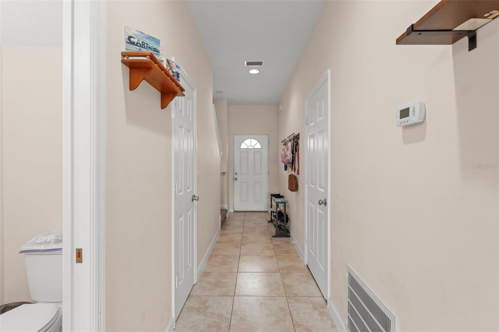 A tiled hallway features white doors, wall-mounted shelves, and a front door at the end — 1880 PETERSON PLACE, SANFORD, FL