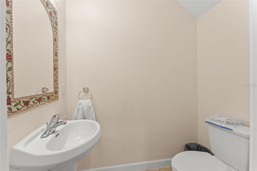 A small bathroom features a pedestal sink, a toilet, and a floral-tiled mirror — 1880 PETERSON PLACE, SANFORD, FL