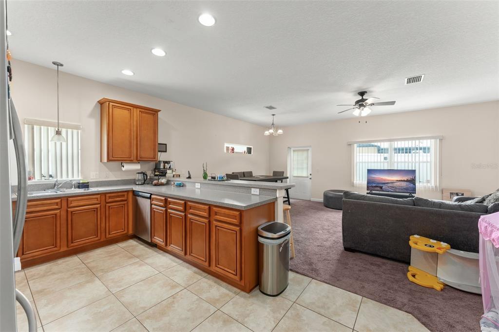 An open-concept kitchen with wood cabinets and a breakfast bar overlooks a carpeted living area — 1880 PETERSON PLACE, SANFORD, FL
