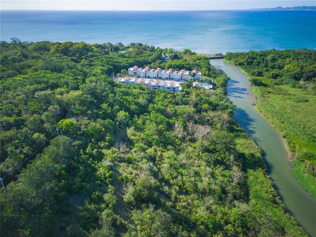 An aerial view shows a multi-story apartment complex surrounded by dense forest and a river — 102 KM 8.2, GUANAJIBO WARD ROAD UNIT C-3, CABO ROJO, PR
