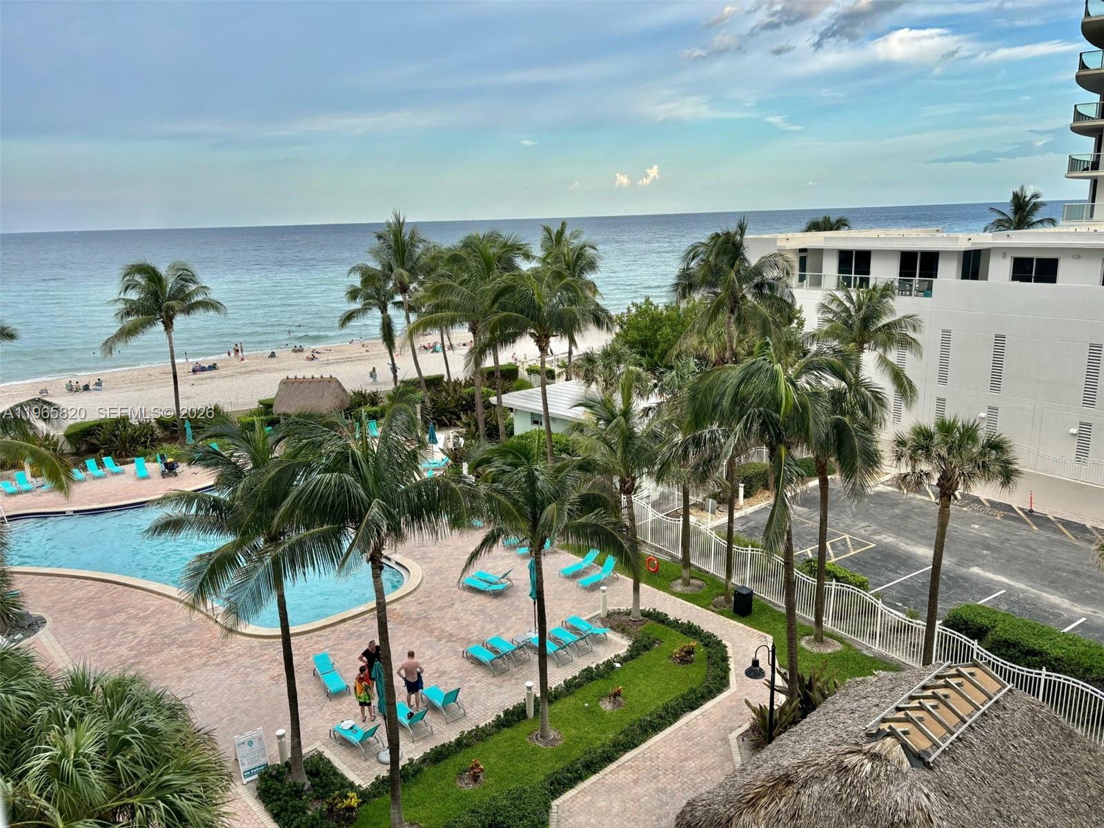 An elevated view of a resort pool area with palm trees, lounge chairs, and beach access — 3901 S Ocean Dr # 5H, Hollywood FL 33019, HOLLYWOOD, FL
