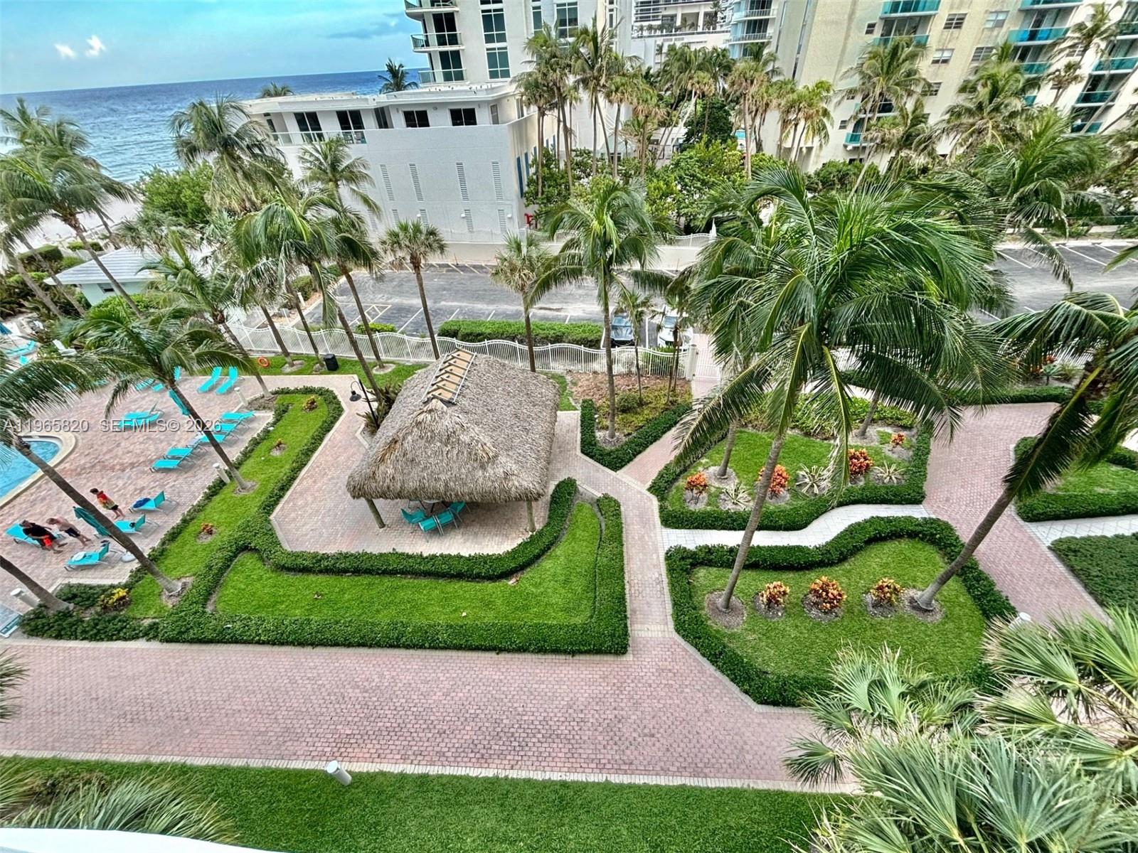 An elevated view of a landscaped courtyard with a tiki hut, pool, and palm trees — 3901 S Ocean Dr # 5H, Hollywood FL 33019, HOLLYWOOD, FL