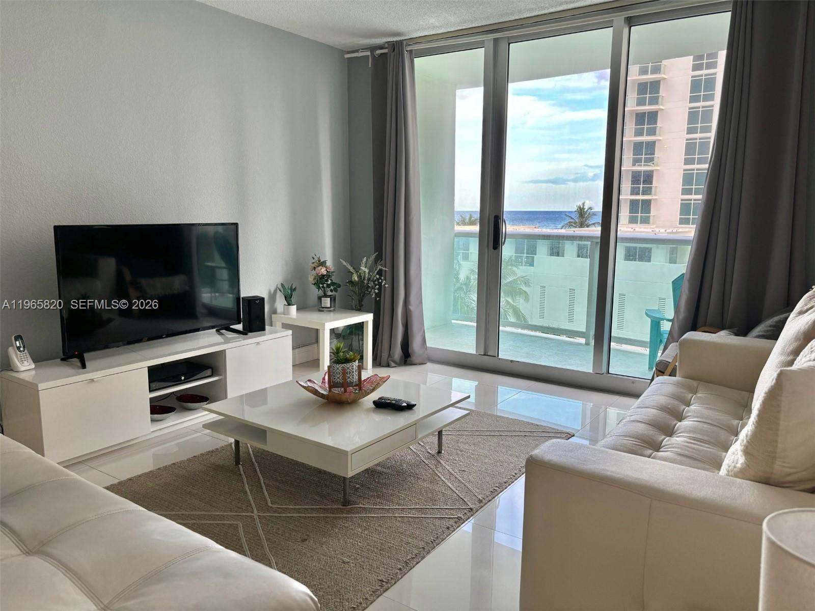 A living room features white tile floors, a white coffee table, and a balcony view — 3901 S Ocean Dr # 5H, Hollywood FL 33019, HOLLYWOOD, FL