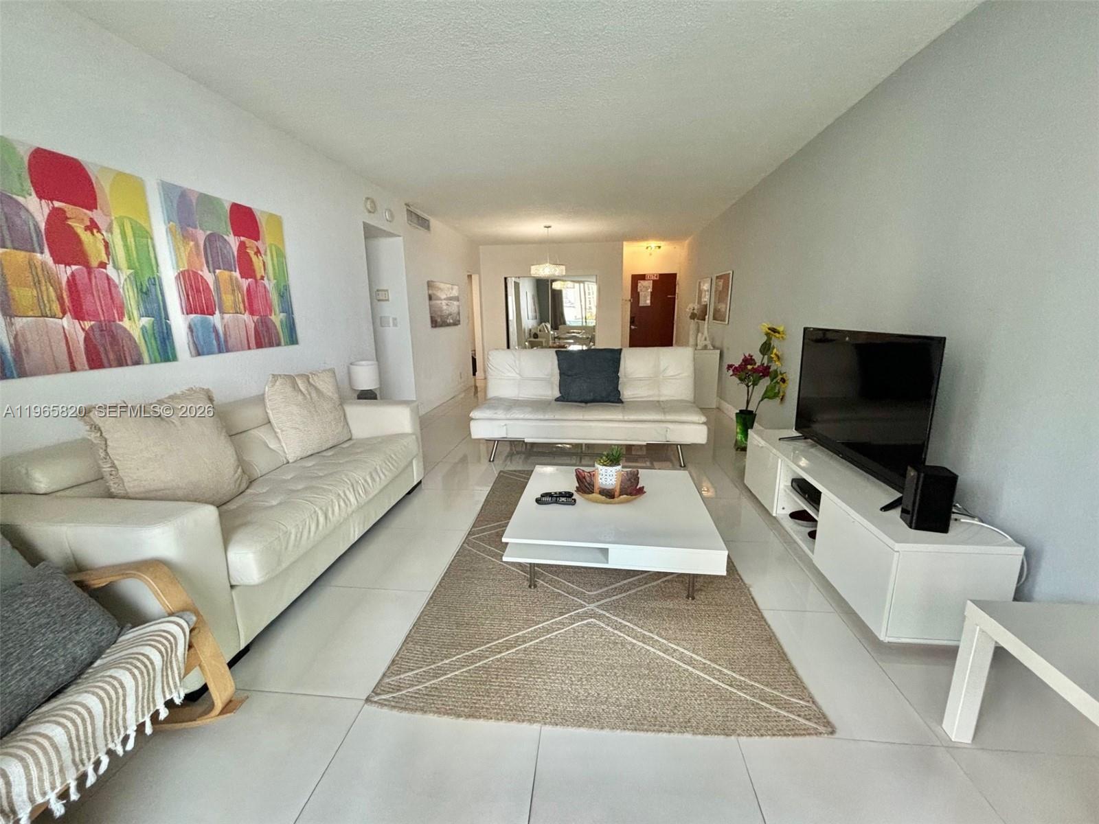 A bright living room features white tile floors, two white sofas, and a central coffee table — 3901 S Ocean Dr # 5H, Hollywood FL 33019, HOLLYWOOD, FL