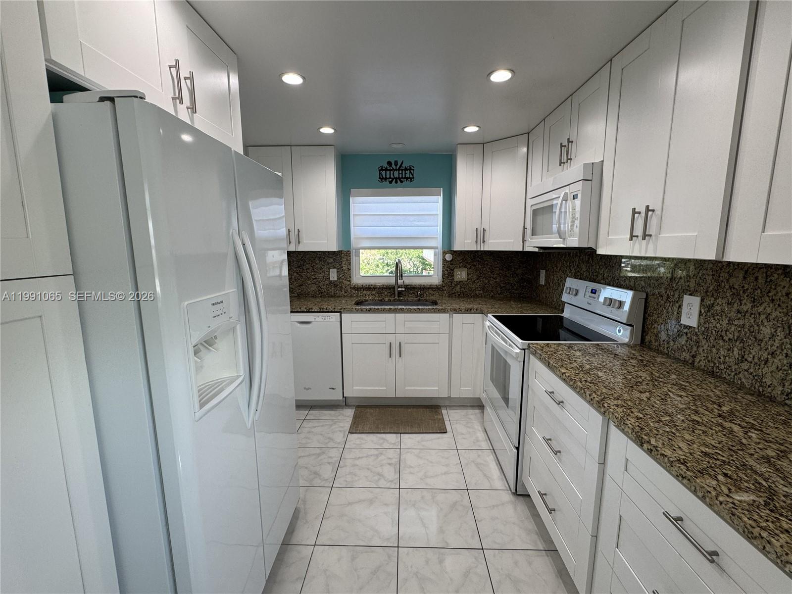 A galley kitchen features white cabinets, granite countertops, stainless steel appliances, and tiled flooring — 5300 Washington St # V407, Hollywood FL 33021, HOLLYWOOD, FL