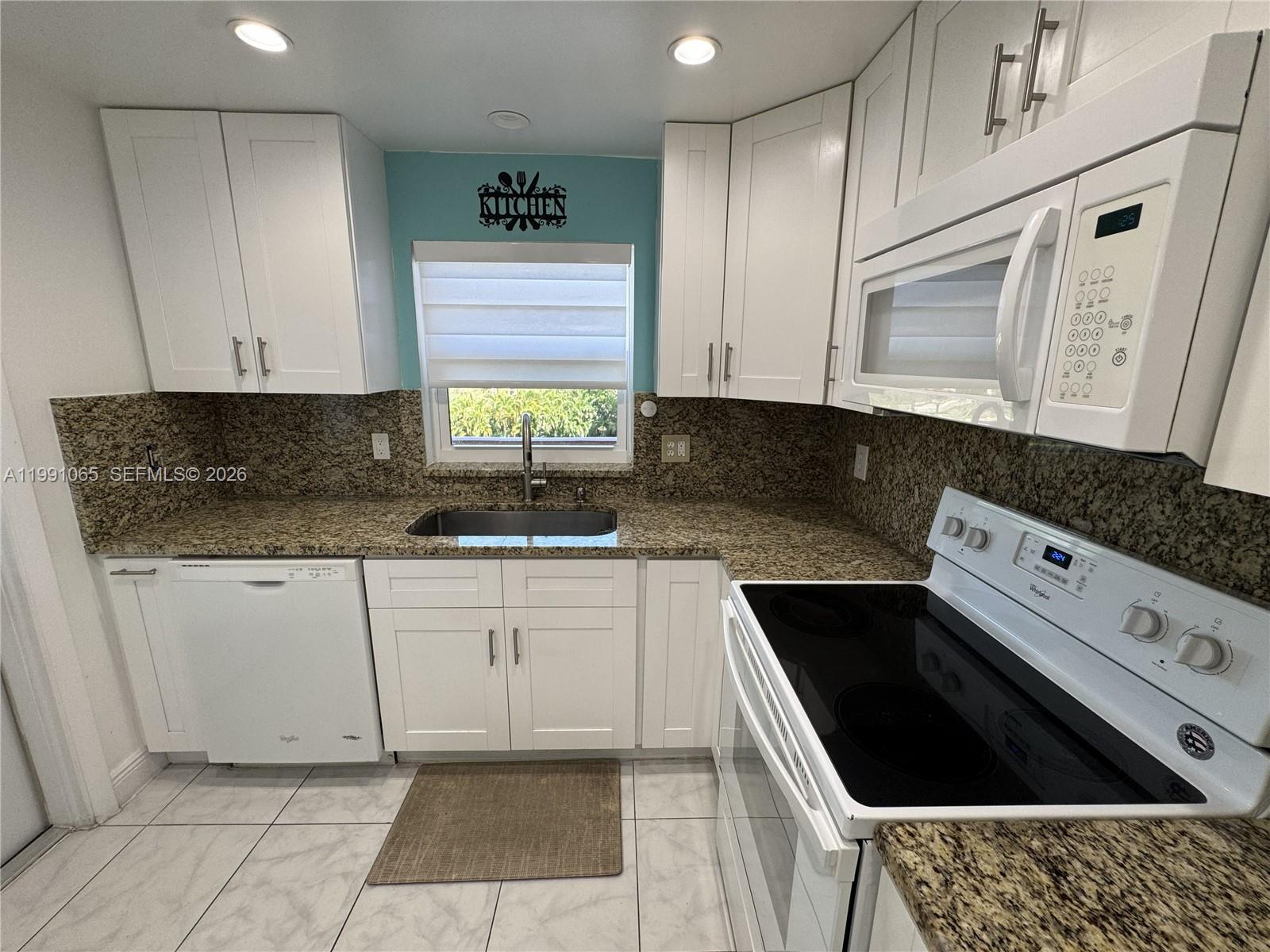 A kitchen features white cabinets, granite countertops, a window, and white appliances — 5300 Washington St # V407, Hollywood FL 33021, HOLLYWOOD, FL