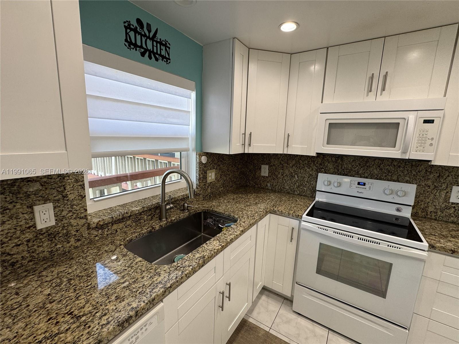 A kitchen features white cabinetry, granite countertops, a stainless steel sink, and white appliances — 5300 Washington St # V407, Hollywood FL 33021, HOLLYWOOD, FL