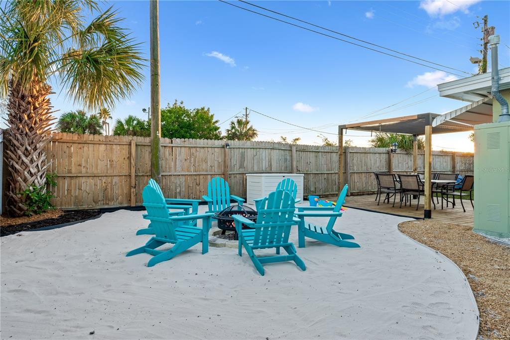 A backyard features a sandy fire pit area with four blue Adirondack chairs and decking — 1225 GROVE STREET, CLEARWATER, FL