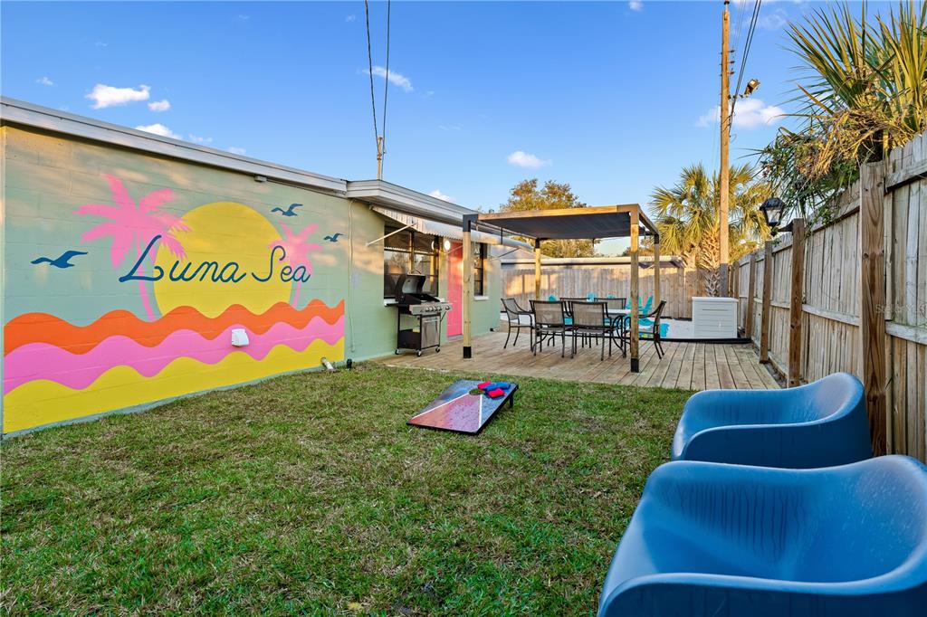 A backyard features a mural-painted wall, a wooden deck with a pergola, and lawn games — 1225 GROVE STREET, CLEARWATER, FL
