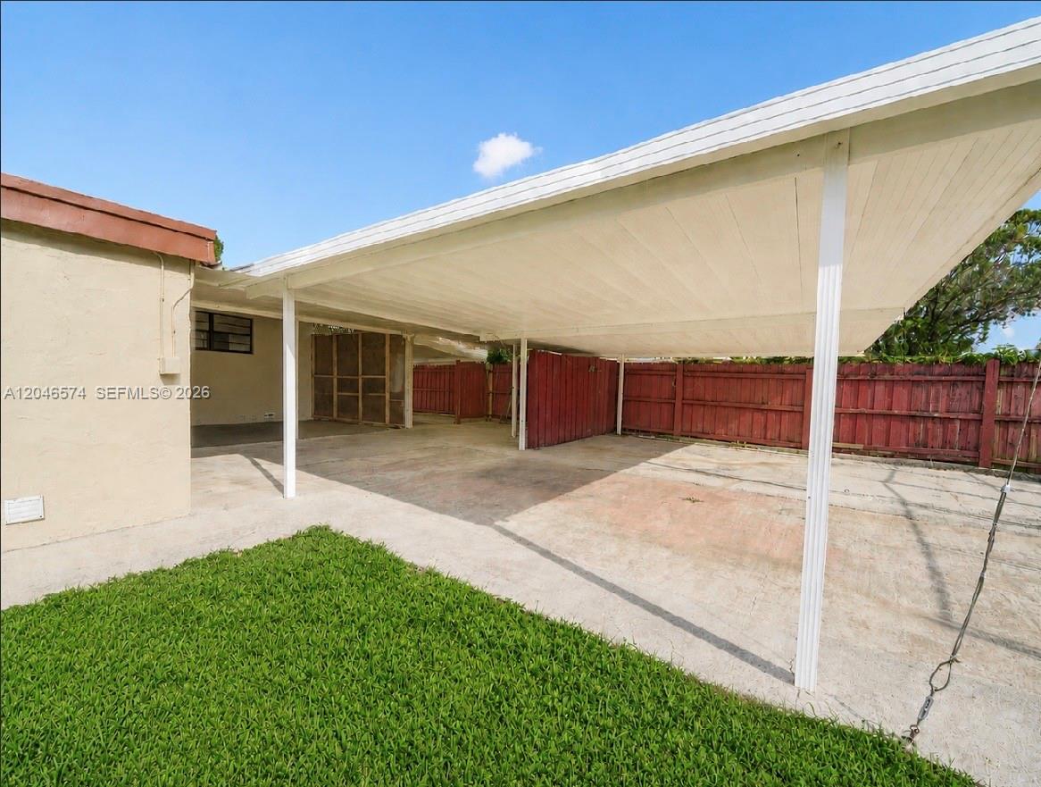 A concrete driveway features a large white metal carport attached to a tan house — 620 NW 182nd Ter, Miami Gardens FL 33169, MIAMI GARDENS, FL