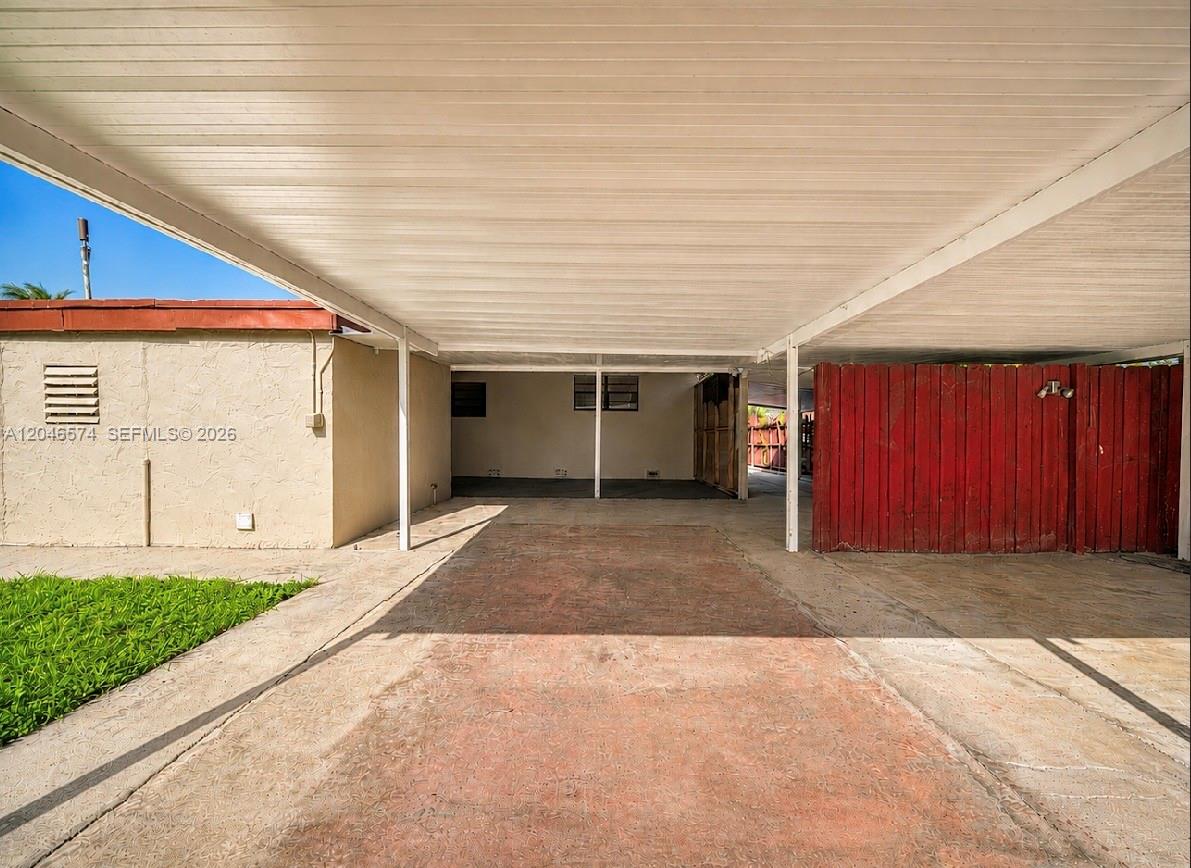A covered carport with a concrete floor and a red wooden privacy fence — 620 NW 182nd Ter, Miami Gardens FL 33169, MIAMI GARDENS, FL