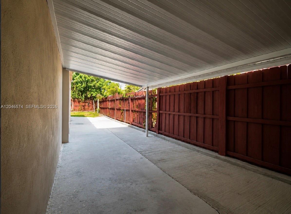 A concrete driveway is covered by a metal carport next to a wooden fence — 620 NW 182nd Ter, Miami Gardens FL 33169, MIAMI GARDENS, FL