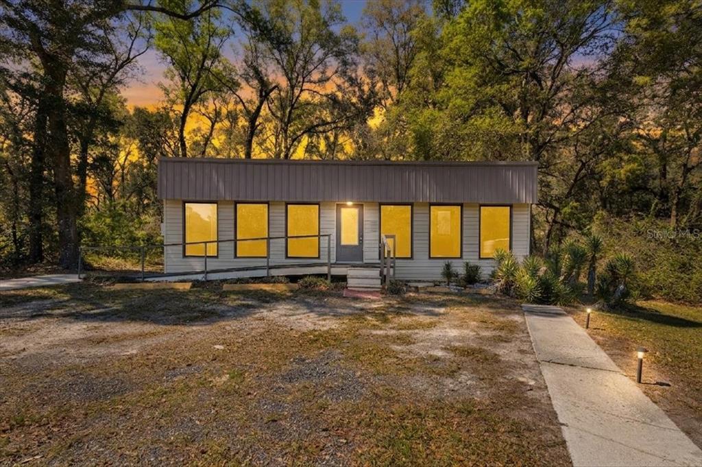 A single-story house with a metal roof, ramp, and large windows sits among trees — 16648 NW US HIGHWAY 19, TRENTON, FL