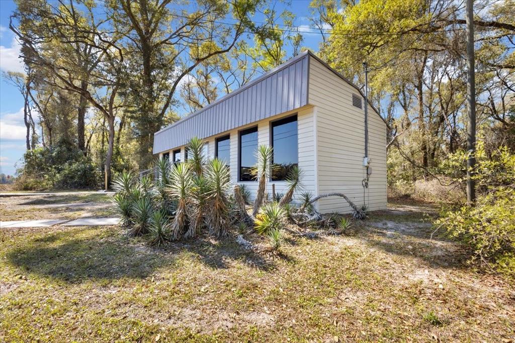 A small, light-colored rectangular building with large windows sits in a wooded, grassy area — 16648 NW US HIGHWAY 19, TRENTON, FL