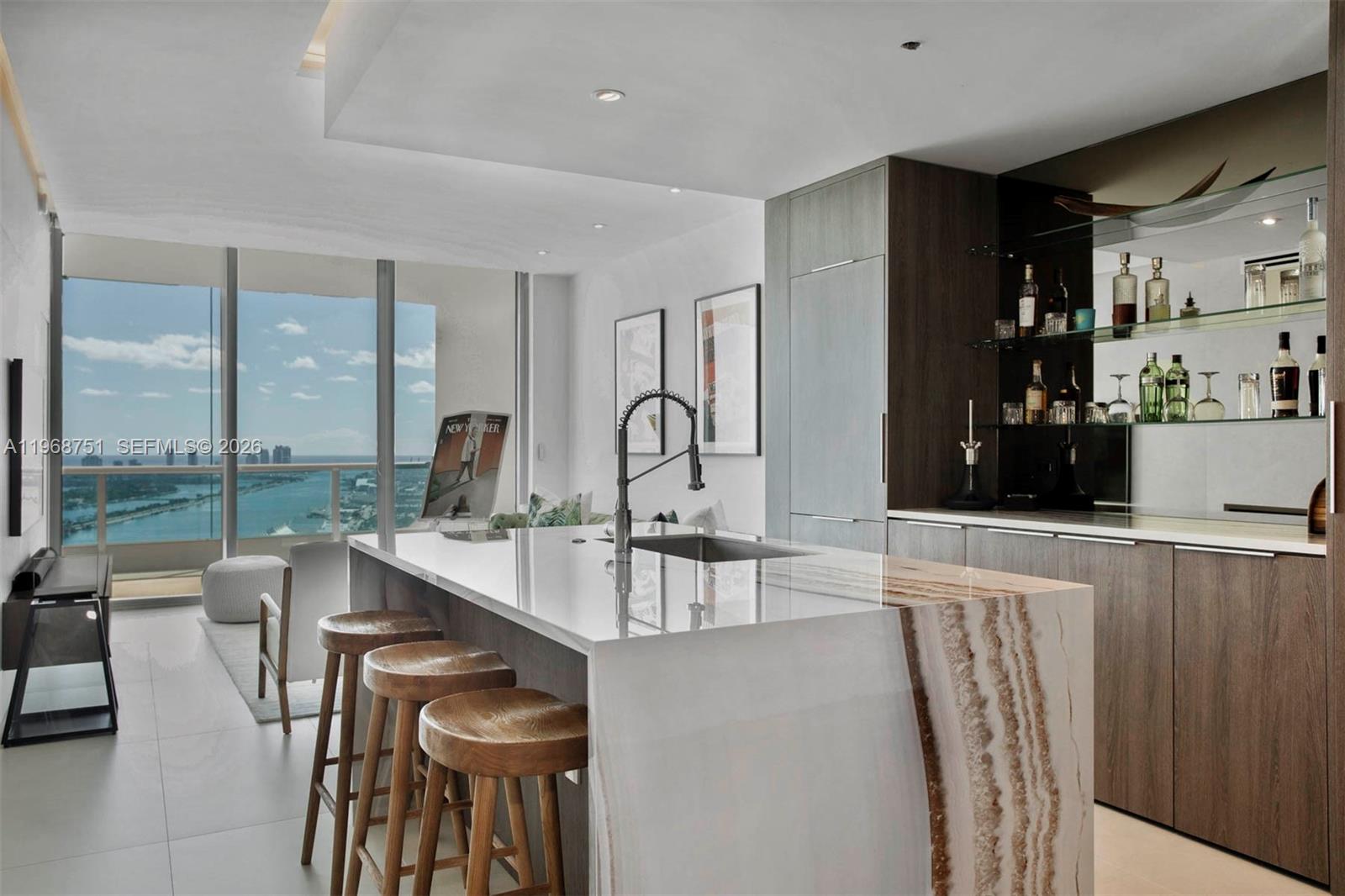 A modern kitchen features a stone waterfall island, wooden bar stools, and a scenic balcony view — 900 Biscayne Blvd # 4307, Miami FL 33132, MIAMI, FL