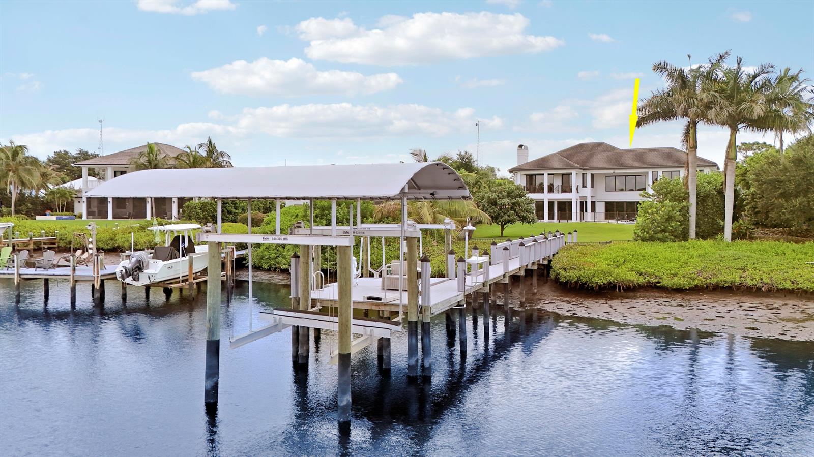 A waterfront house with a boat dock and lift sits on a grassy lawn — 18411 SE Lakeside Drive, Jupiter FL 33469, JUPITER, FL