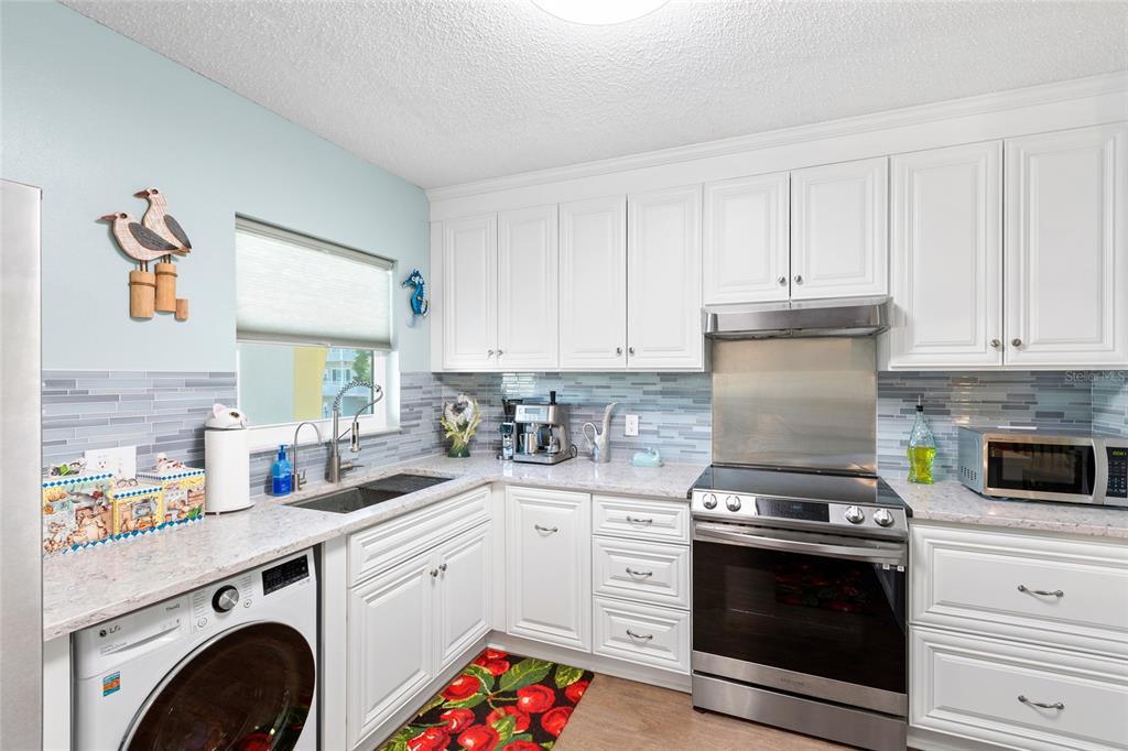 A kitchen features white cabinets, a stainless steel stove, a tiled backsplash, and a washing machine — 2259 COSTA RICAN DRIVE UNIT 23, CLEARWATER, FL