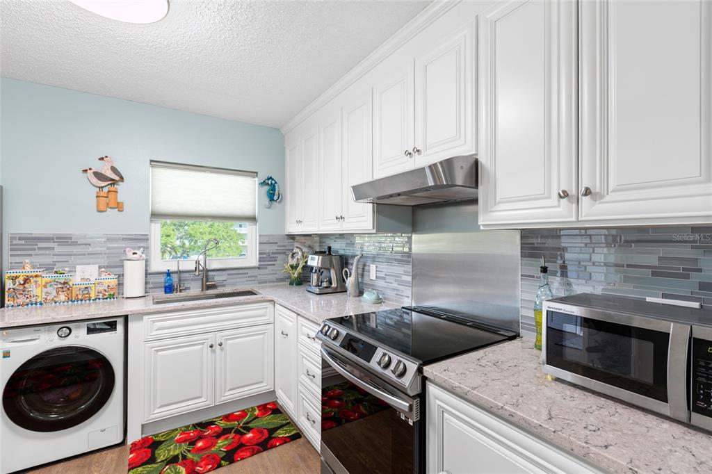 A kitchen features white cabinets, a stainless steel range, a built-in washer, and gray backsplash — 2259 COSTA RICAN DRIVE UNIT 23, CLEARWATER, FL