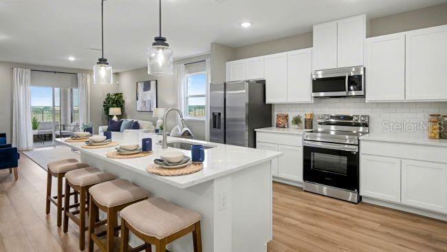 A modern kitchen features white cabinets, stainless steel appliances, and a large island with seating — 207 MARION OAKS MANOR, OCALA, FL