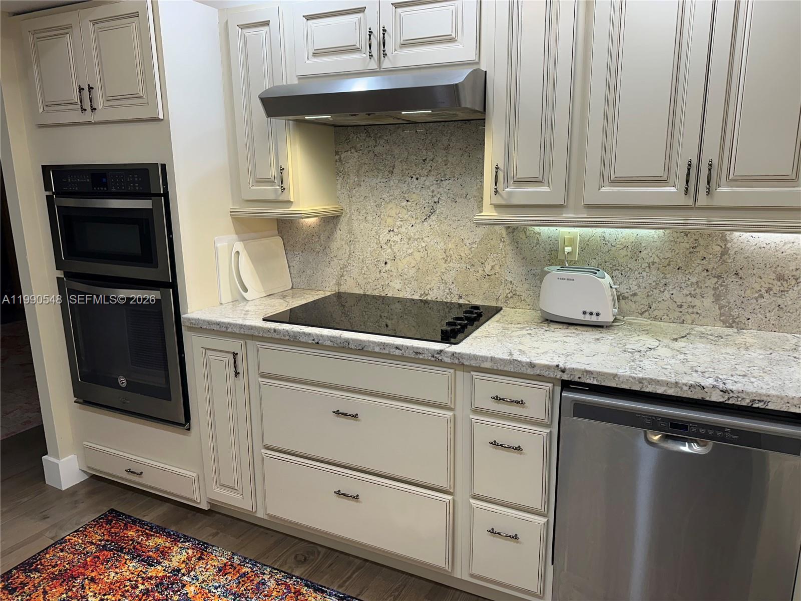 A kitchen features cream-colored cabinets, granite countertops, a stainless steel oven, and a glass cooktop — 6039 Collins Ave # 1431, Miami Beach FL 33140, MIAMI BEACH, FL