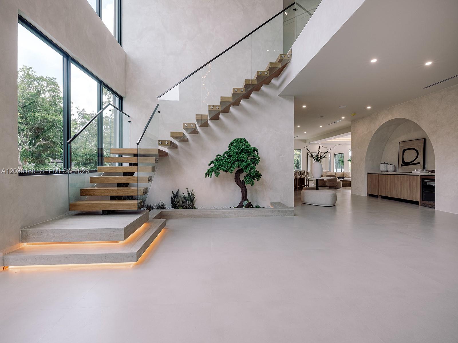 A spacious modern dining area features a floating staircase, indoor landscaping, and floor-to-ceiling windows — 9530 SW 95th Ct, Miami FL 33176, MIAMI, FL