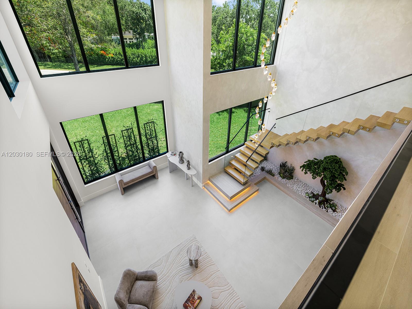A high-ceilinged modern foyer features a floating staircase, a small indoor tree, and large windows — 9530 SW 95th Ct, Miami FL 33176, MIAMI, FL