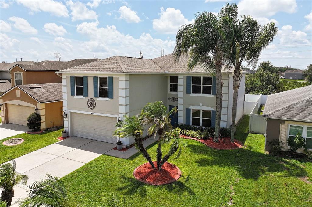A two-story suburban house with a tan stucco exterior, a garage, and palm trees — 1424 AGUACATE COURT, ORLANDO, FL