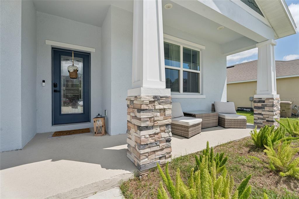 A covered front porch features stone-based columns, wicker seating, and a dark blue front door — 4902 PALL MALL STREET E, KISSIMMEE, FL