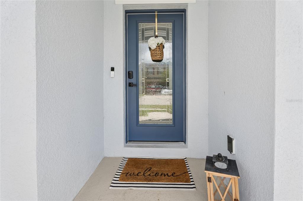 A blue front door with a glass insert and a welcome mat on a porch — 4902 PALL MALL STREET E, KISSIMMEE, FL