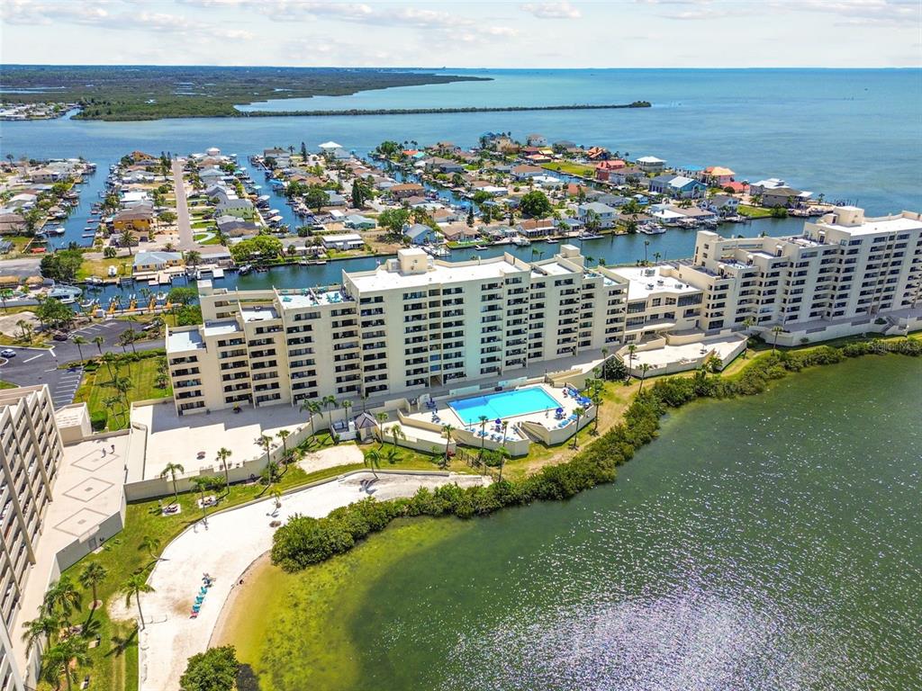 An aerial view shows a large waterfront apartment complex with a pool and sandy beach — 6009 SEA RANCH DRIVE UNIT 107, HUDSON, FL