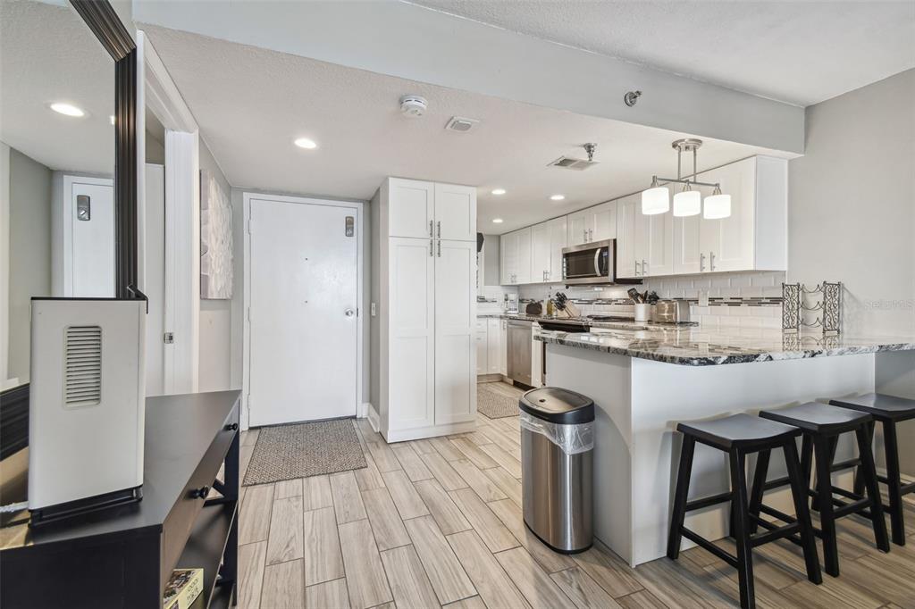 A kitchen with white cabinets, granite countertops, and a breakfast bar with three stools — 6009 SEA RANCH DRIVE UNIT 107, HUDSON, FL