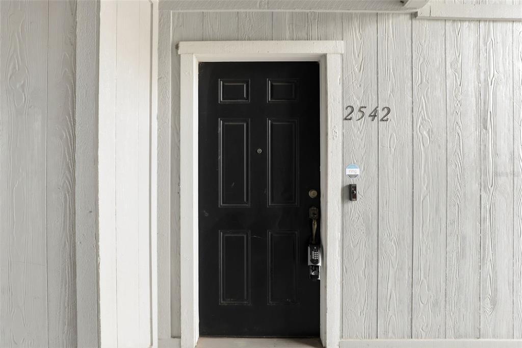 A black front door with a digital lock is set into a light-colored wood-paneled wall — 2542 OAK PARK WAY UNIT 101, ORLANDO, FL