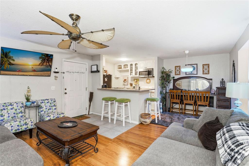 An open-concept living room and kitchen featuring wood flooring, a ceiling fan, and bar seating — 2542 OAK PARK WAY UNIT 101, ORLANDO, FL