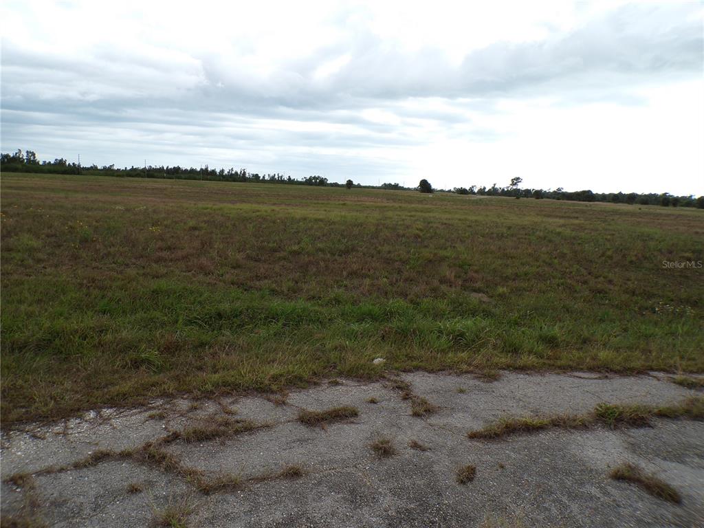 A large, flat, grassy field is viewed from the edge of a paved road — 1 BOBOLINK PLACE, PLACIDA, FL