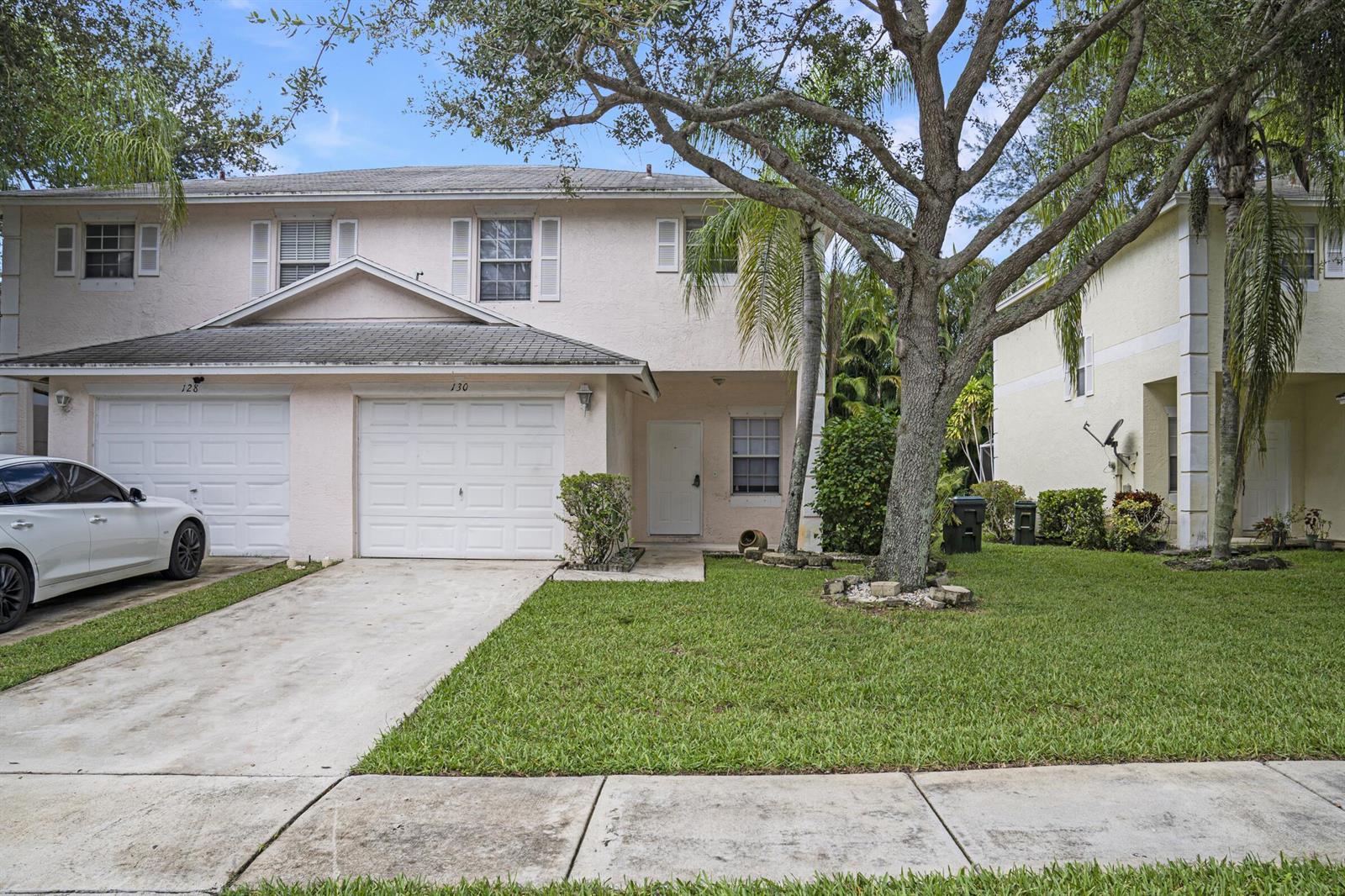 A two-story townhouse with a white garage, light-colored stucco exterior, and a front lawn — 130 Baldwin Boulevard, FL 33463, FL