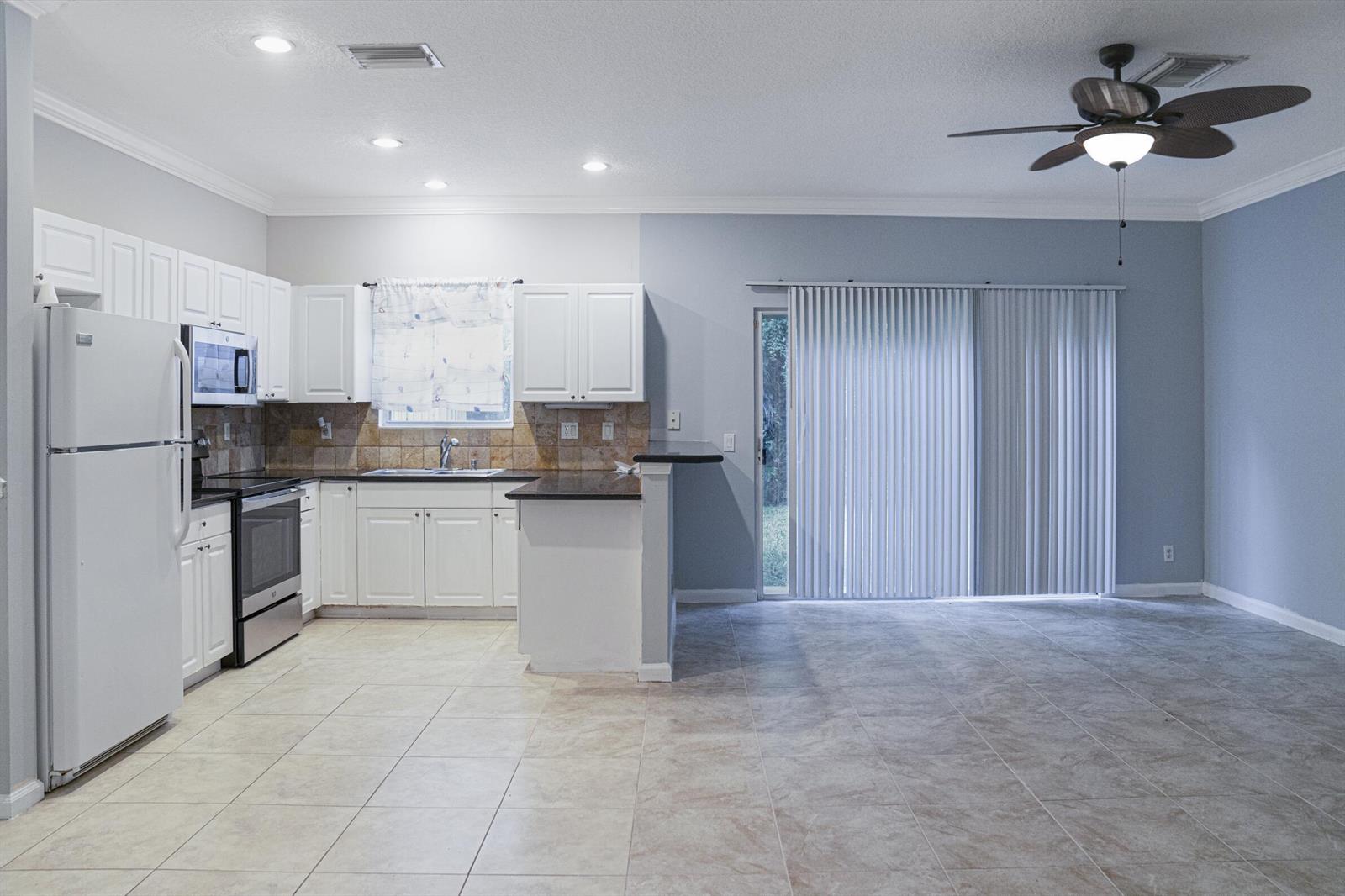 A kitchen with white cabinets, stainless steel appliances, and tile flooring opens to a living area — 130 Baldwin Boulevard, FL 33463, FL