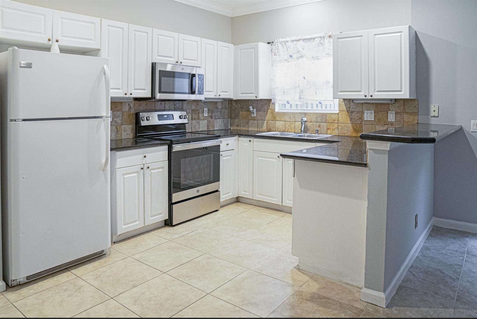 A kitchen features white cabinets, stainless steel appliances, dark countertops, and a tiled backsplash — 130 Baldwin Boulevard, FL 33463, FL