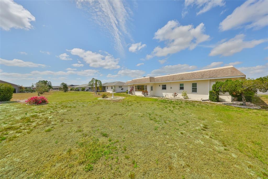 A wide, grassy backyard features a single-story house with a light-colored exterior and a fountain — 1529 ALLEGHENY DRIVE, SUN CITY CENTER, FL