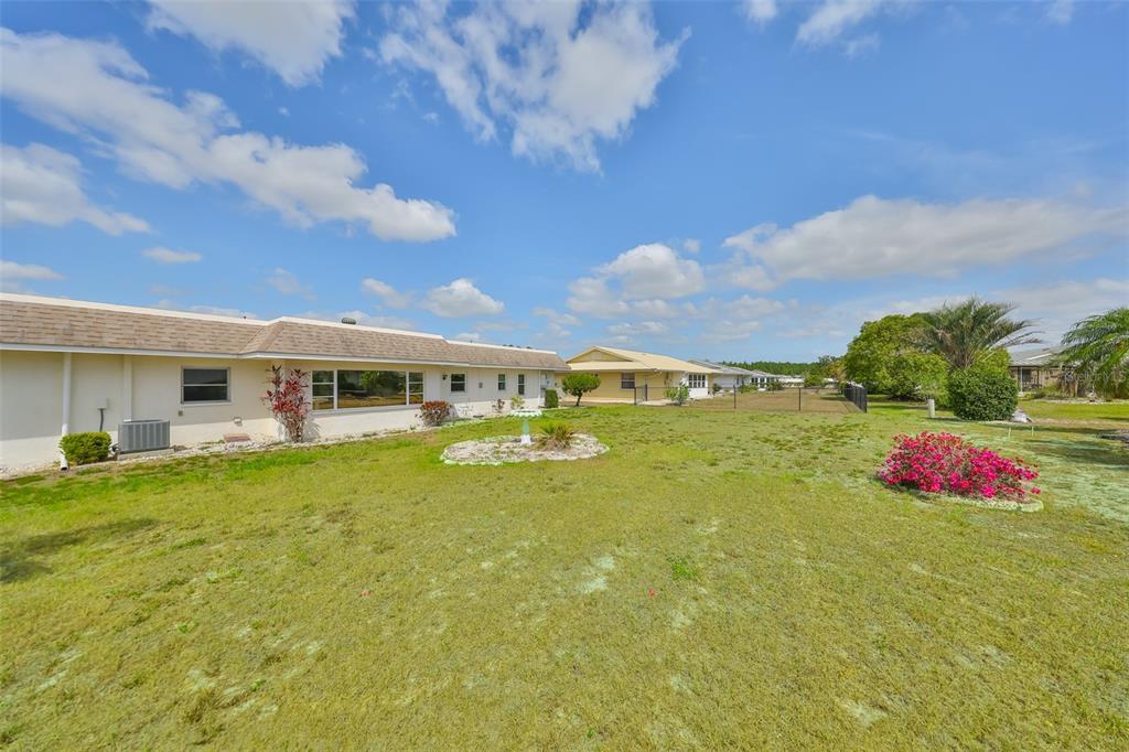 A view of a backyard with a tan house, green lawn, and a small garden — 1529 ALLEGHENY DRIVE, SUN CITY CENTER, FL