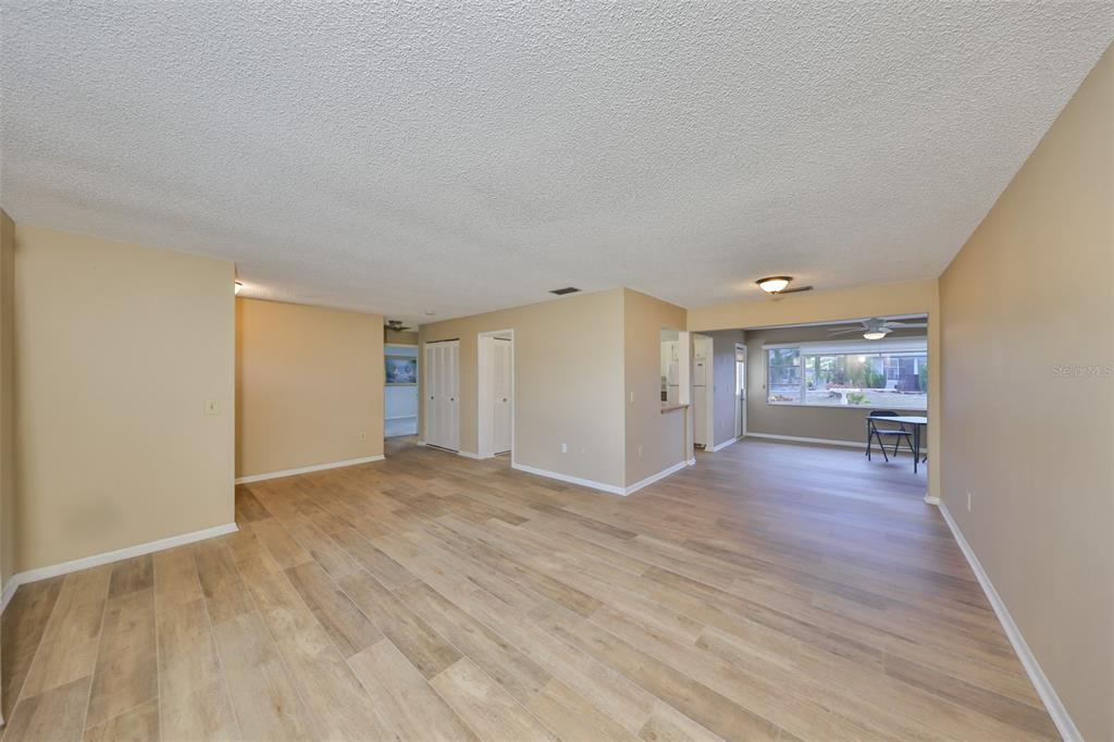 An open-concept living area features light wood-look flooring, beige walls, and a textured ceiling — 1529 ALLEGHENY DRIVE, SUN CITY CENTER, FL