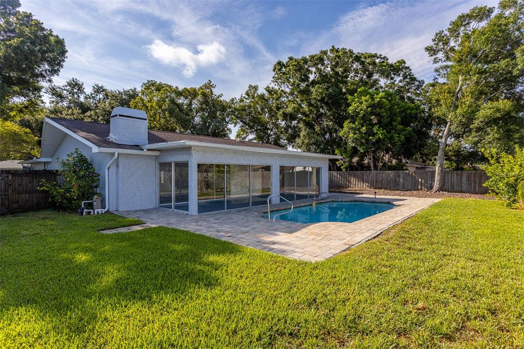 A backyard view of a house with a screened-in porch, swimming pool, and stone patio — 3276 FOX HILL DRIVE, CLEARWATER, FL