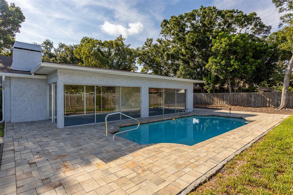 A backyard features a swimming pool with a metal handrail next to a glass-enclosed patio — 3276 FOX HILL DRIVE, CLEARWATER, FL