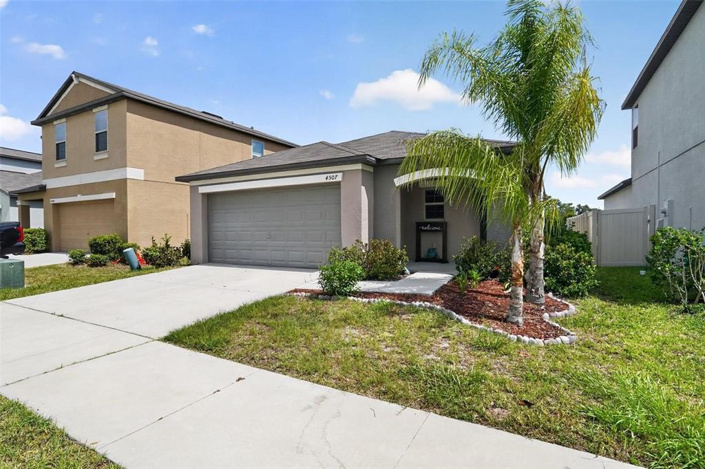 A single-story suburban house with a gray garage, a palm tree, and a concrete driveway — 4507 ETERNAL PRINCE DRIVE, SUN CITY CENTER, FL