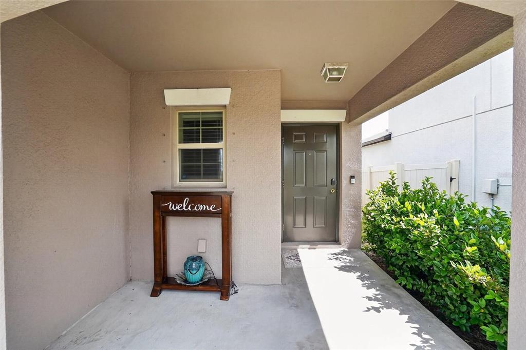 A covered entryway features a concrete floor, a brown front door, and a welcome table — 4507 ETERNAL PRINCE DRIVE, SUN CITY CENTER, FL