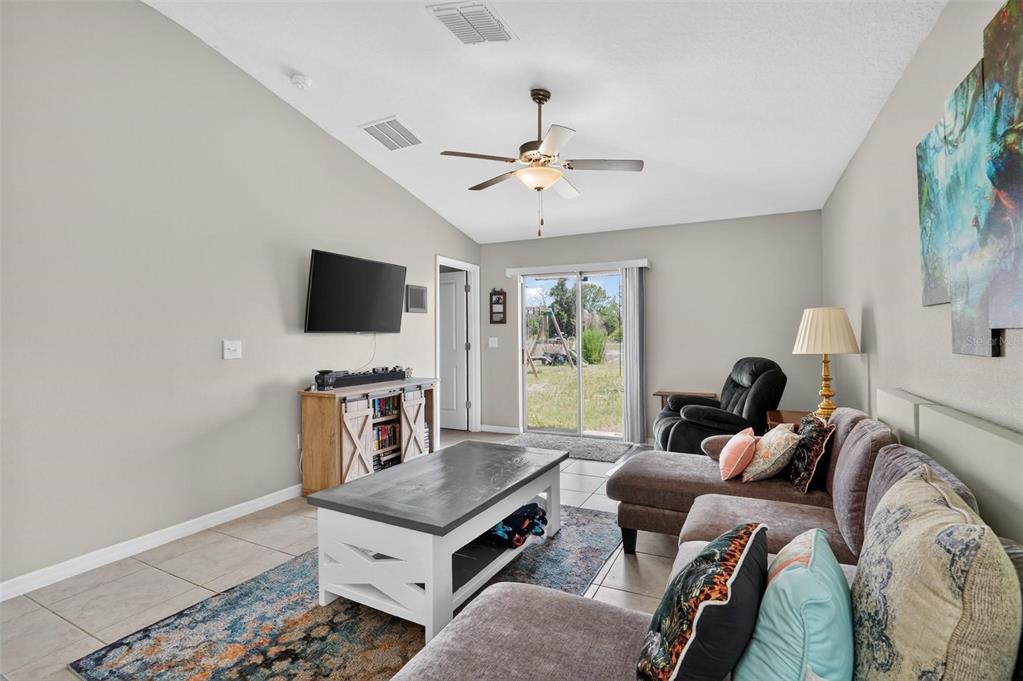 A living room features a vaulted ceiling, tile flooring, a sectional sofa, and sliding glass doors — 4507 ETERNAL PRINCE DRIVE, SUN CITY CENTER, FL