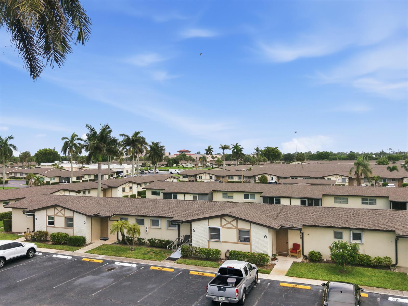 An aerial view shows a residential complex with single-story buildings, palm trees, and parking spaces — 2789 Ashley Drive W # C, West Palm Beach FL 33415, WEST PALM BEACH, FL