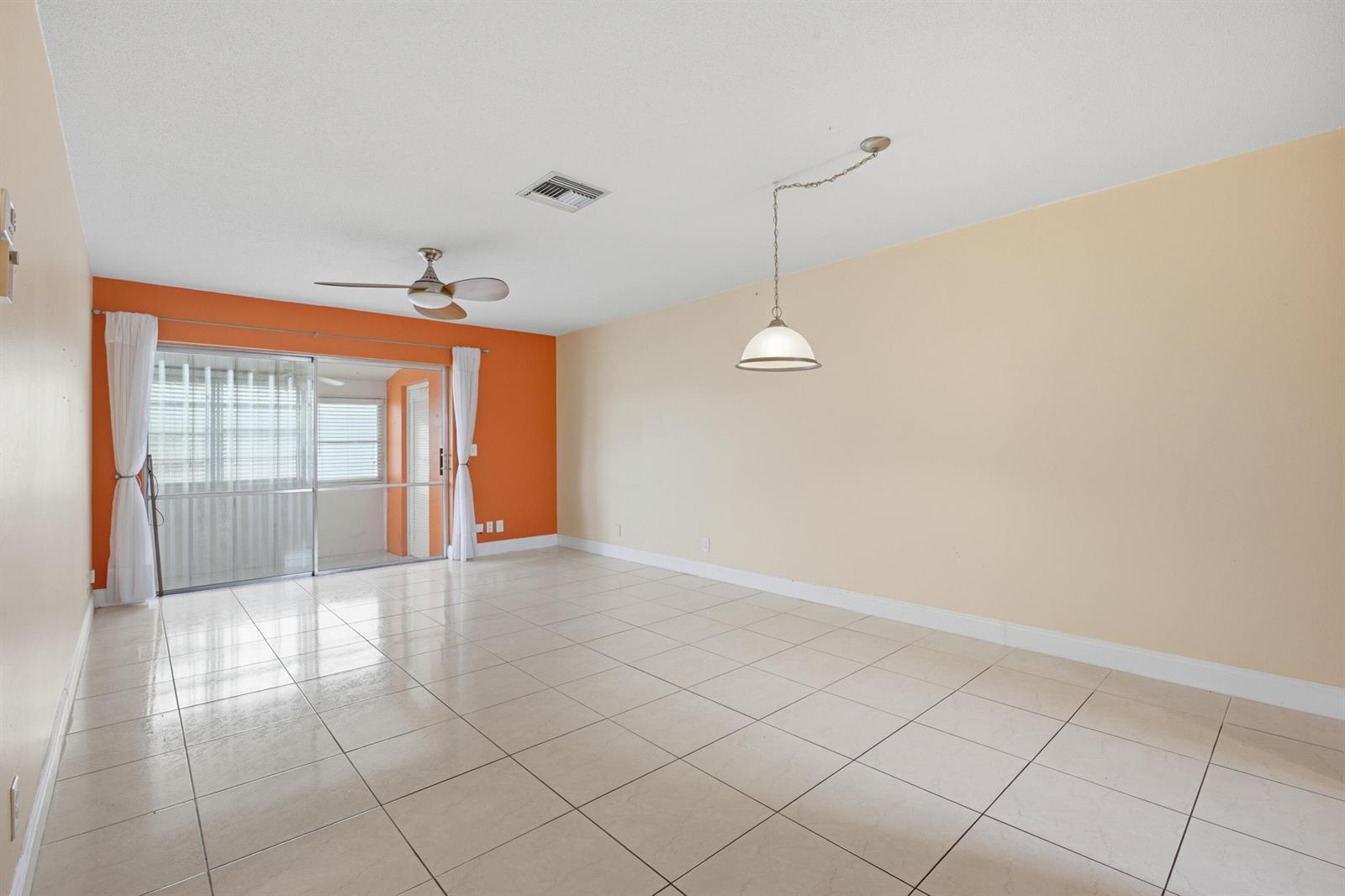 An empty room features beige tile floors, an orange accent wall, and a sliding glass door — 2789 Ashley Drive W # C, West Palm Beach FL 33415, WEST PALM BEACH, FL